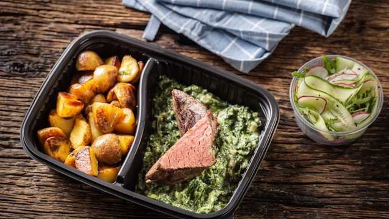 A plastic container with potatoes, steak and salad