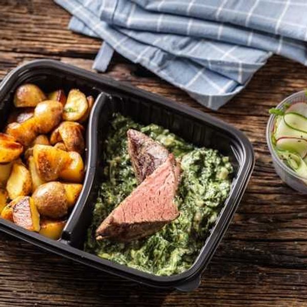 A plastic container with potatoes, steak and salad