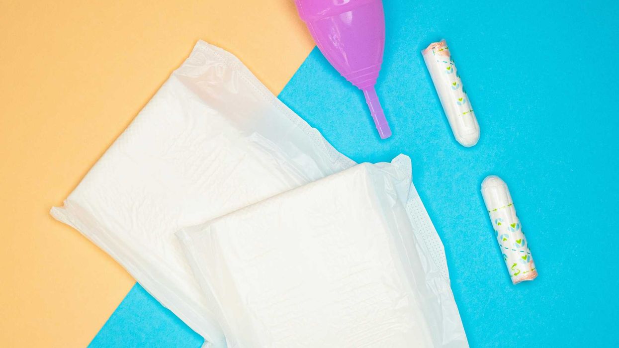 A plastic menstrual cup, tampons and menstrual pads on a blue and orange surface.