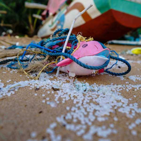 A plastic toy sitting near plastic nurdles on a sandy beach