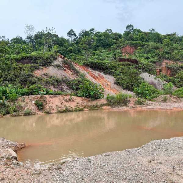 A pool of water next to hillsides with green vegetation and bare earth patches.