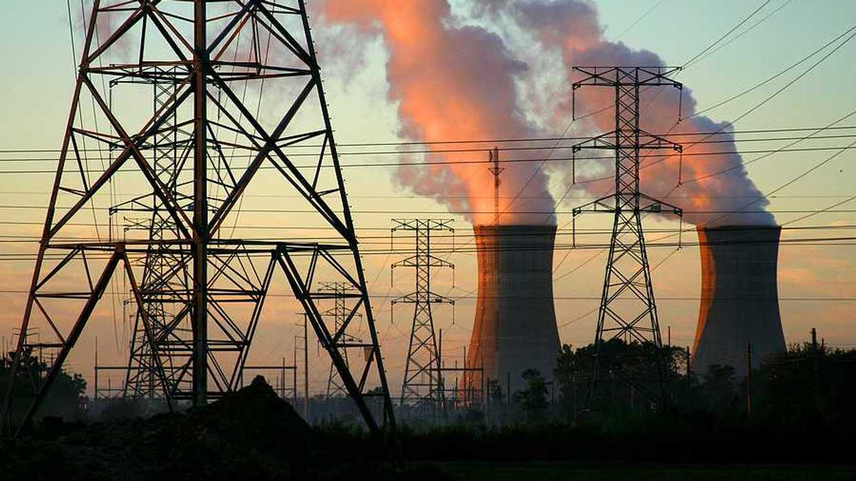 A power plant with smoke billowing from towers with electric energy lines in the foreground