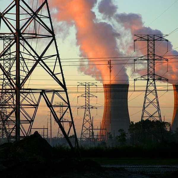 A power plant with smoke billowing from towers with electric energy lines in the foreground