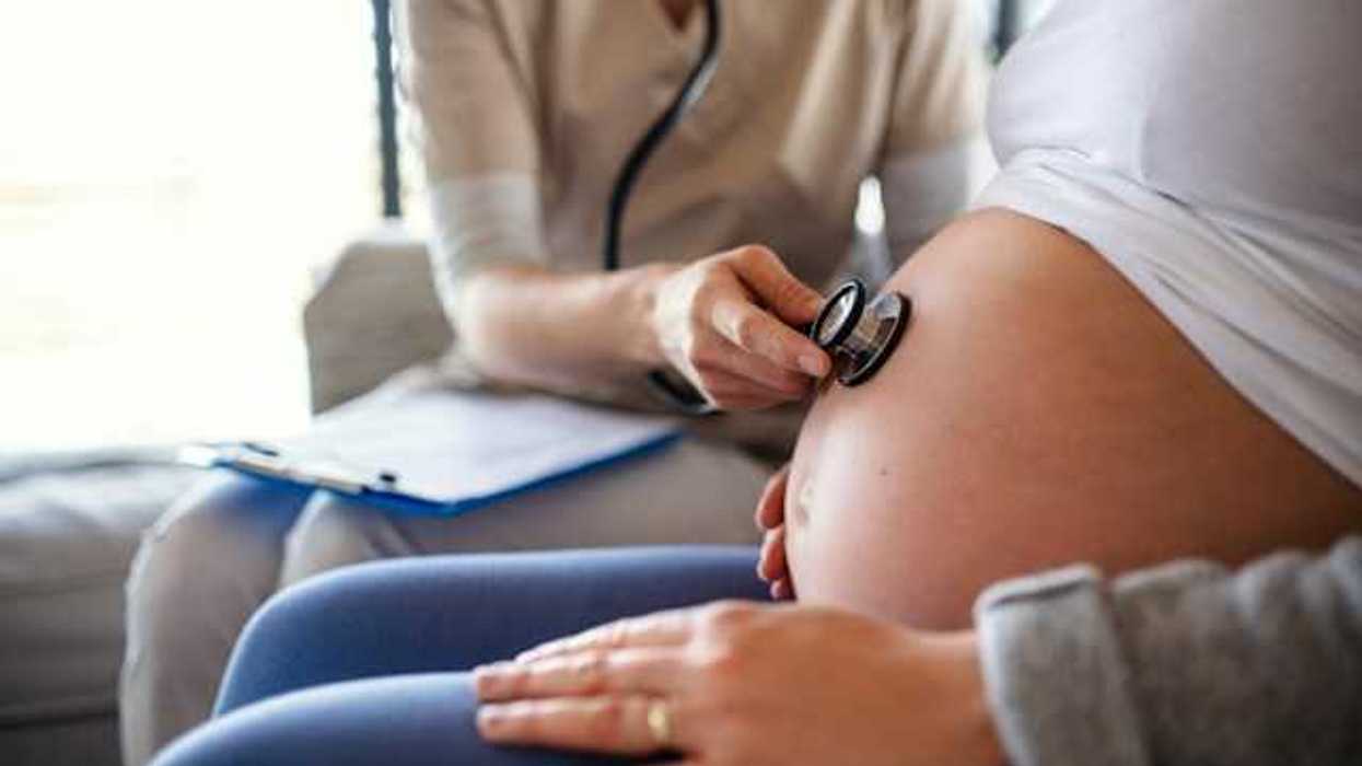 A pregnant woman sitting in a chair with a doctor using a stethoscope to listen to her baby's heart beat through her belly