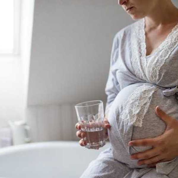A pregnant woman wearing a robe and holding a glass of water