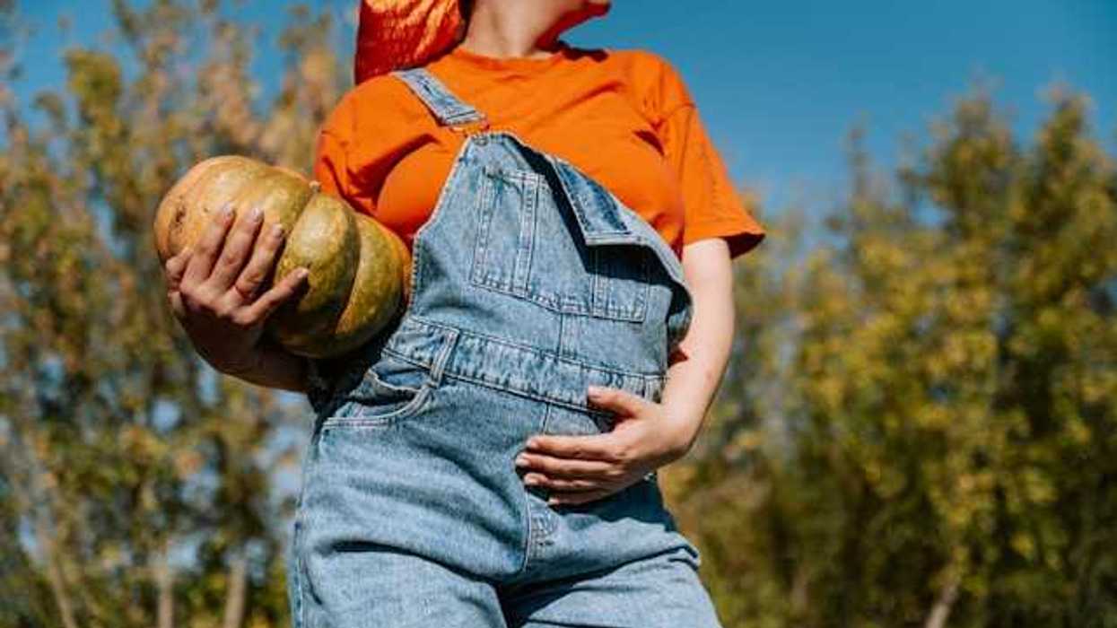 A pregnant woman wearing overalls and holding her belly, with a squash in her arms