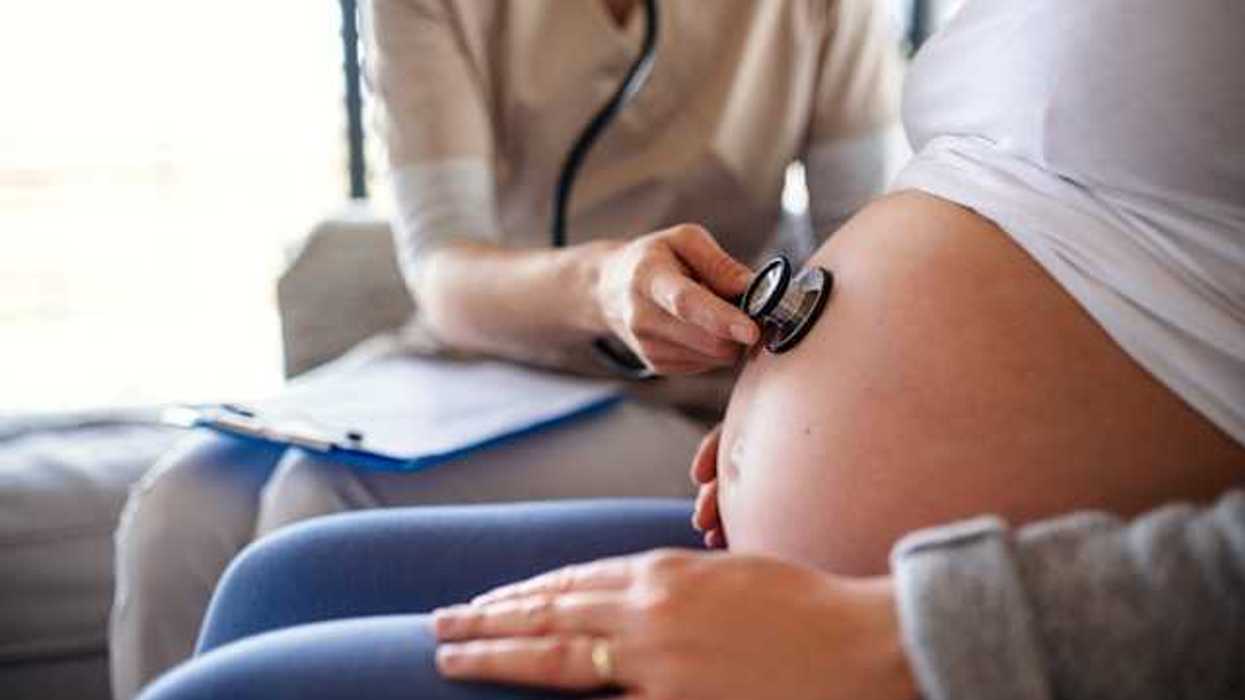 A pregnant woman with a person holding a stethoscope to her belly