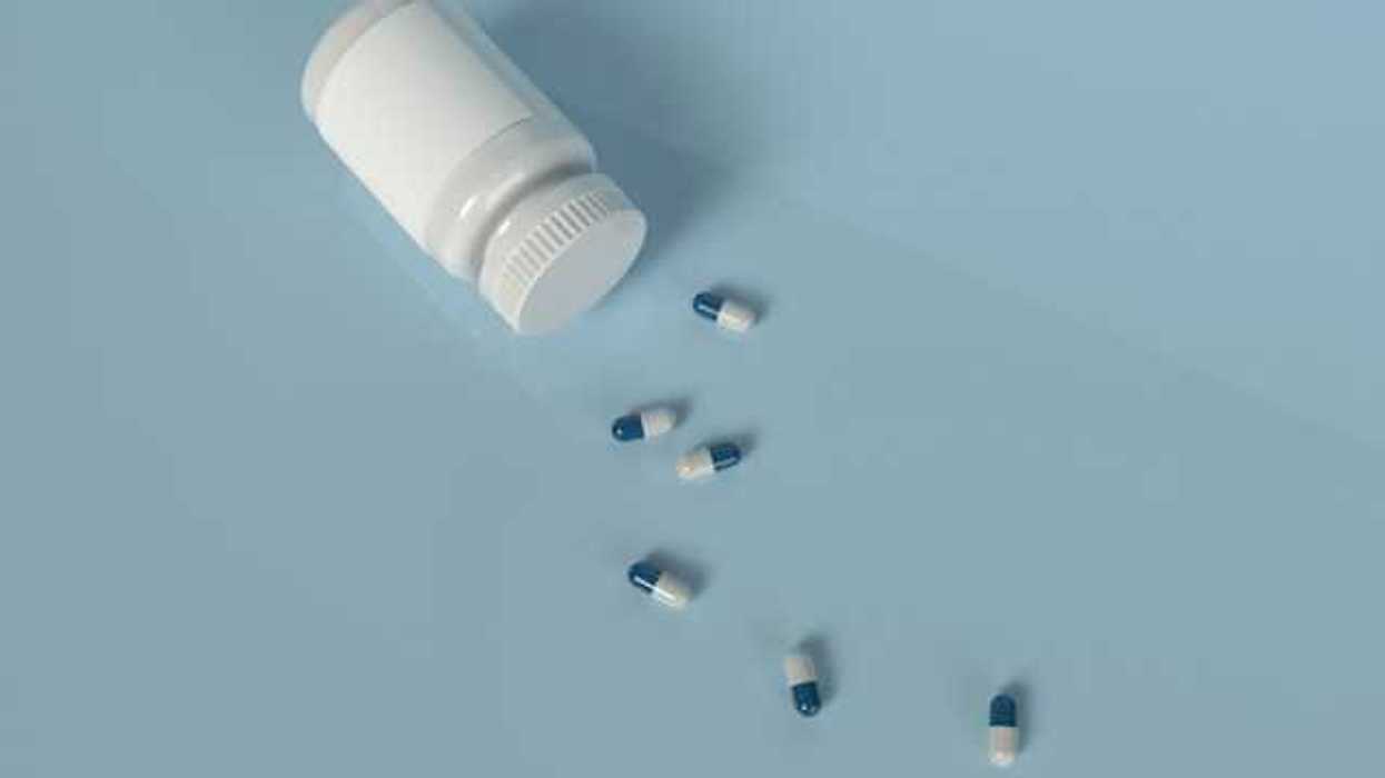 A prescription bottle with blue and white pills laying on a light blue background