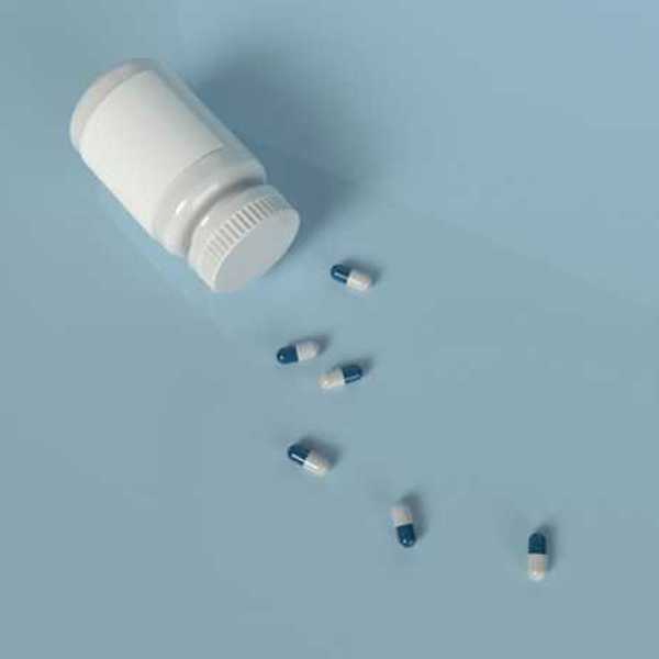 A prescription bottle with blue and white pills laying on a light blue background