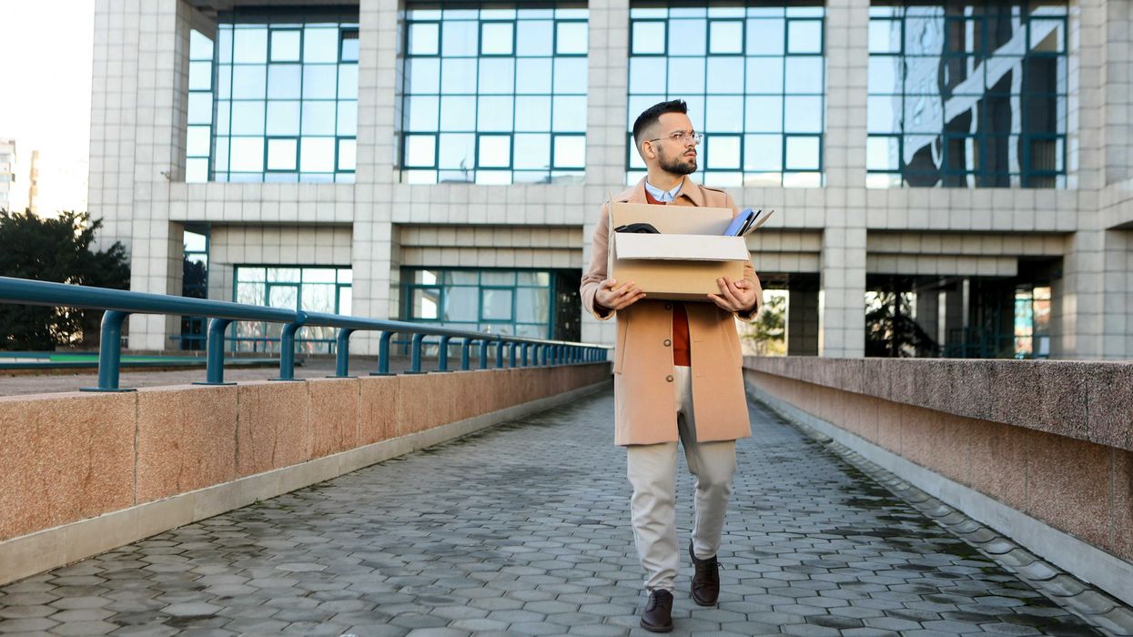 A professional man leaves an office building carrying a box of office supplies.