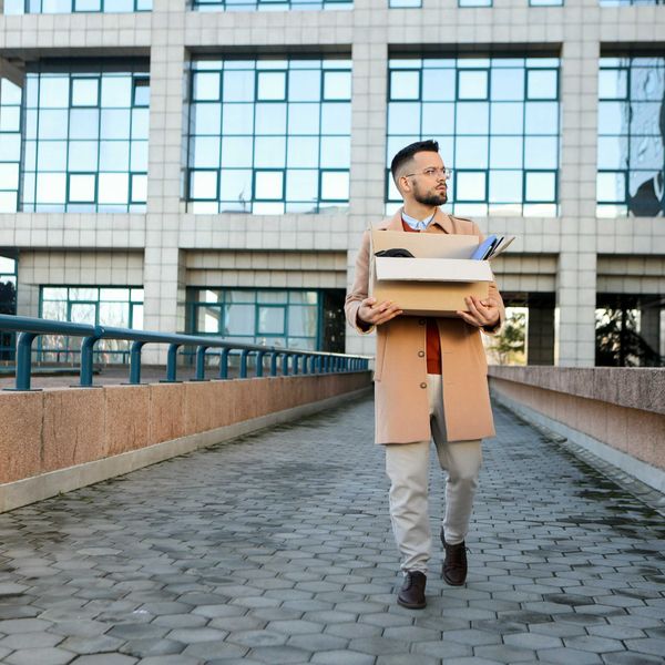 A professional man leaves an office building carrying a box of office supplies.