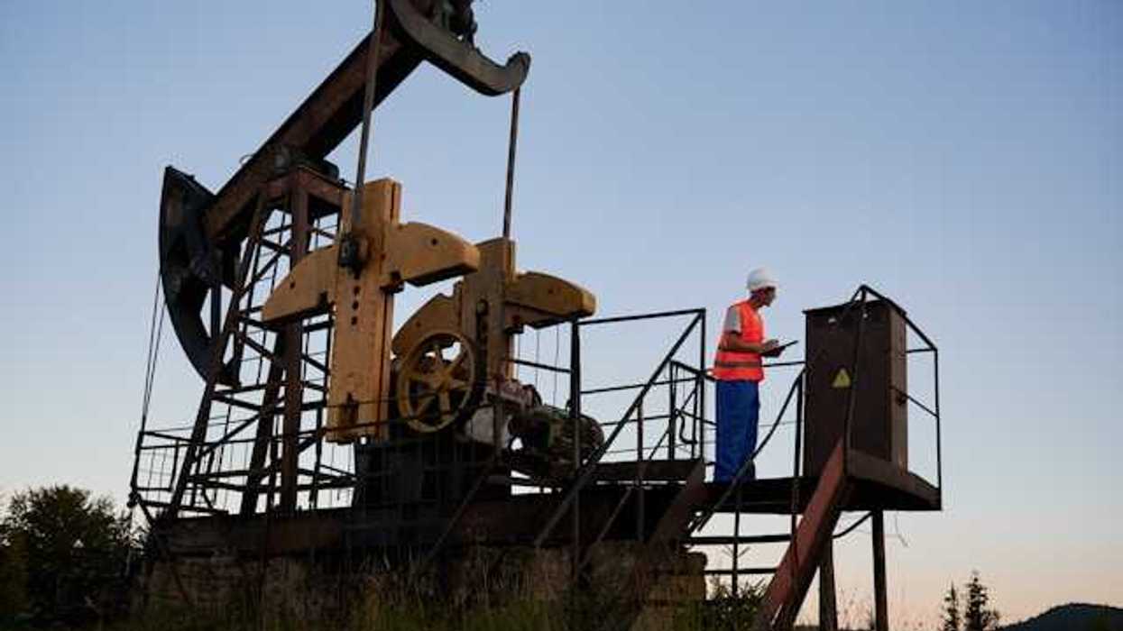 A pump jack with a maintenance worker on a platform next to it