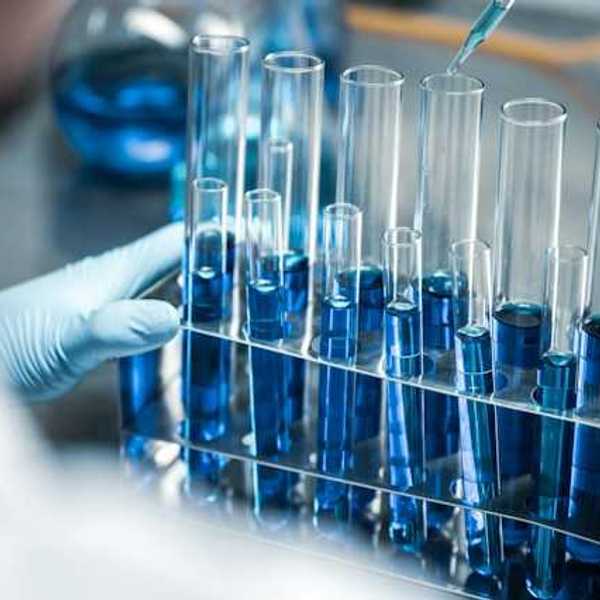 A rack of test tubes with blue liquid in them, with a lab worker using a dropper in one of them