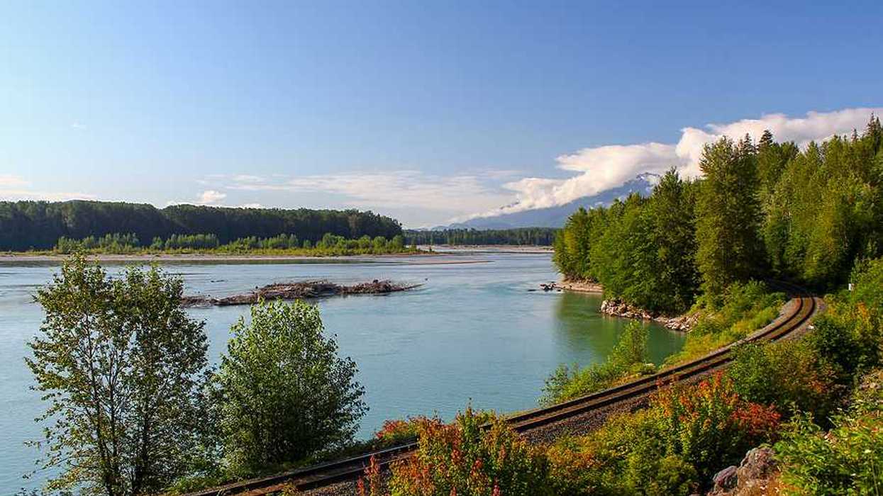 A railway line extending past a lake with trees and mountains in the background