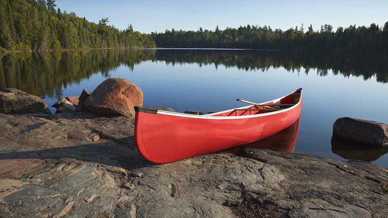 A red canoe sitting on the edge of a lake