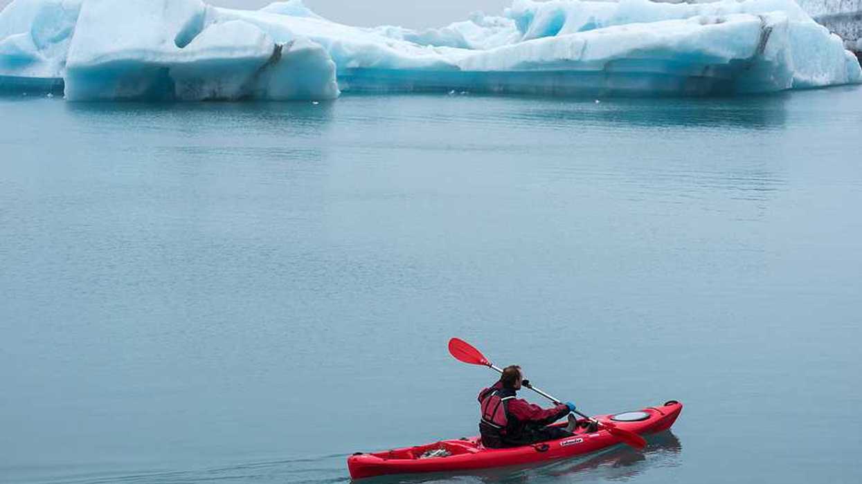 A red kayak with a person in it paddling past ice bergs