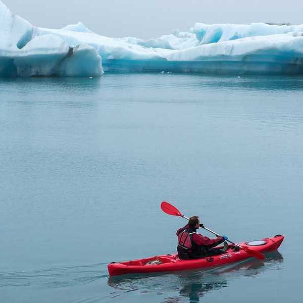 A red kayak with a person in it paddling past ice bergs