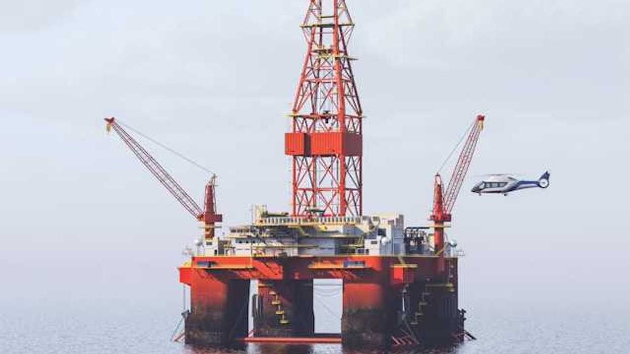 A red offshore oil drill with a helicopter flying near it