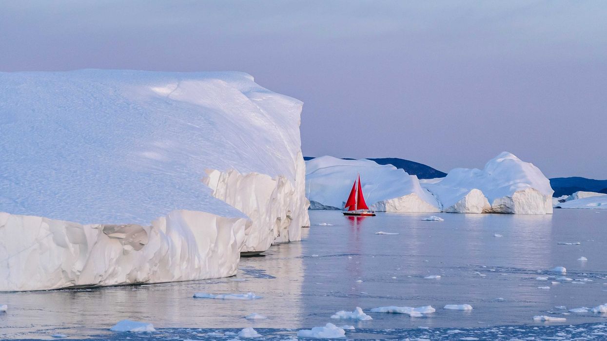 A red sailboat in the water near icebergs