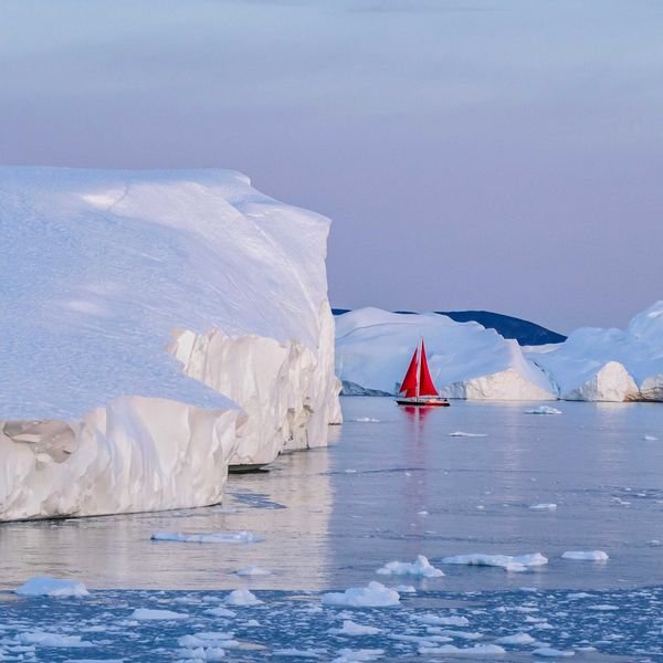A red sailboat in the water near icebergs