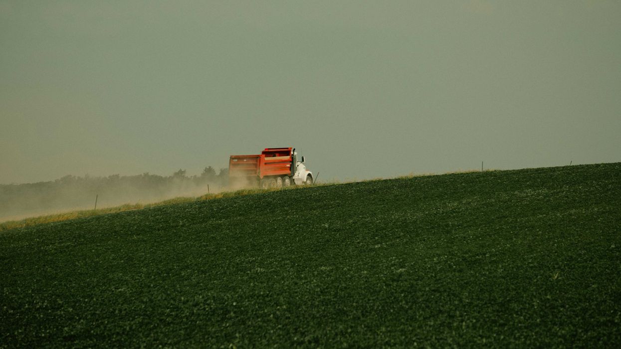 a red truck driving next to a lush green farm field
