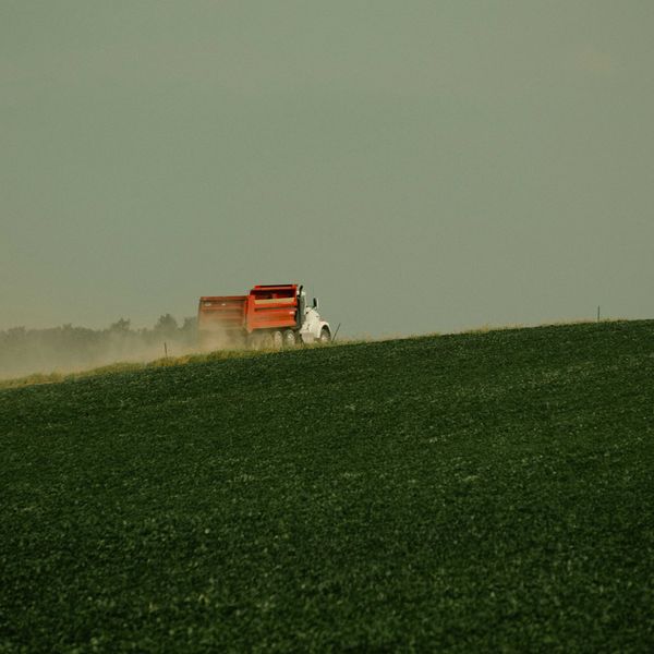 a red truck driving next to a lush green farm field