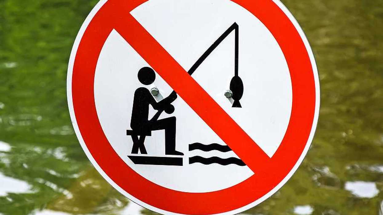 A red, white and black sign indicating that fishing is prohibited with a body of water in the background