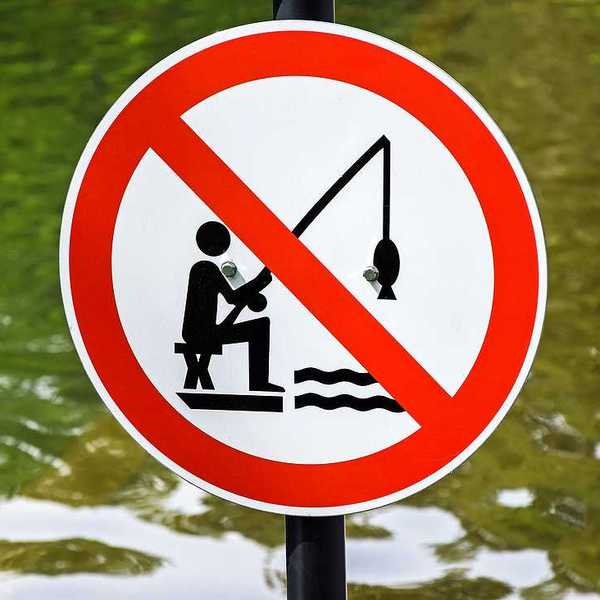 A red, white and black sign indicating that fishing is prohibited with a body of water in the background