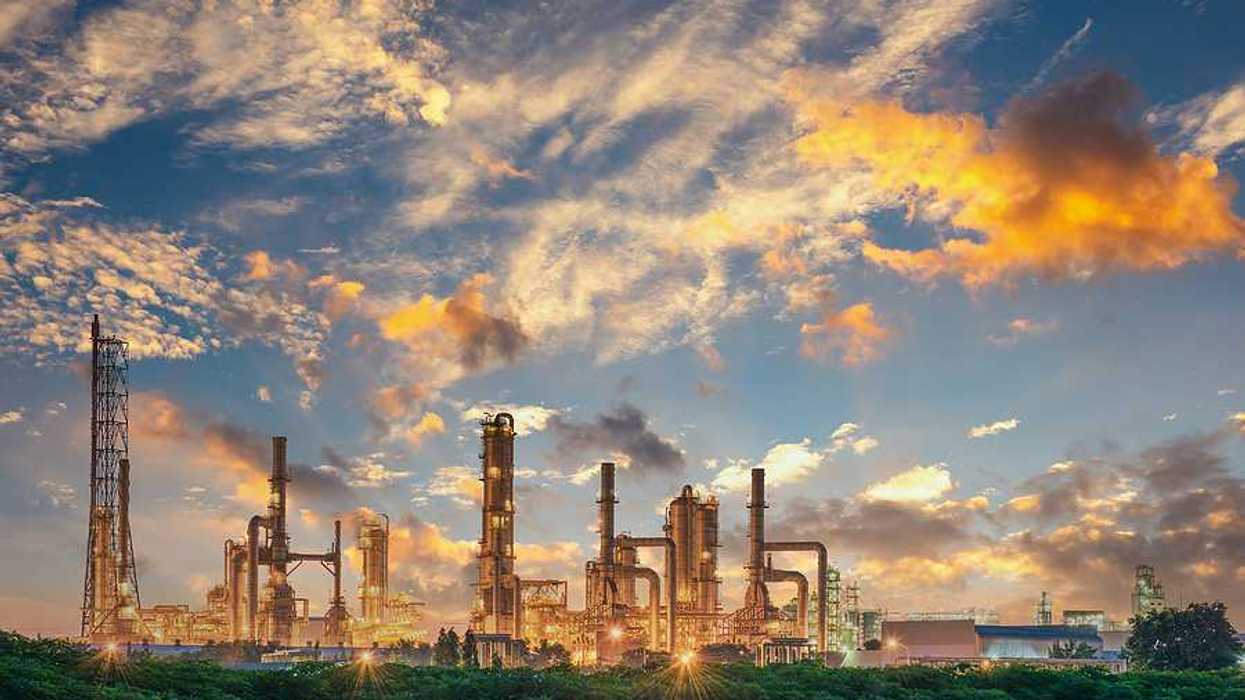 A refinery under a sunset with green trees in the foreground