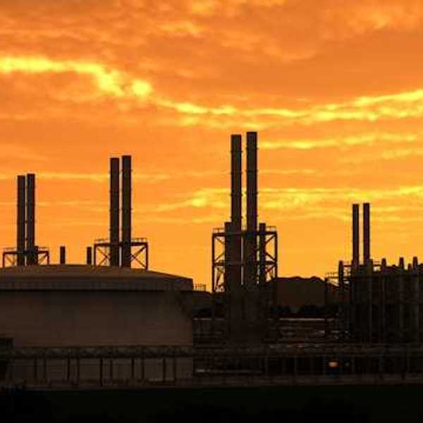 A refinery with smokestacks silhouetted against a sunset sky