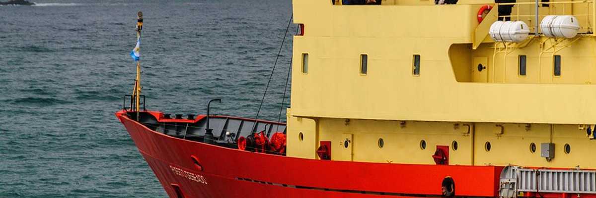 A research vessel in the sea with icy mountains in the background.