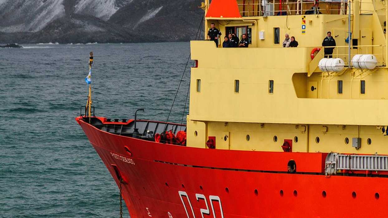A research vessel in the sea with icy mountains in the background.