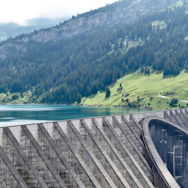 A reservoir with a dam with green mountains in the background