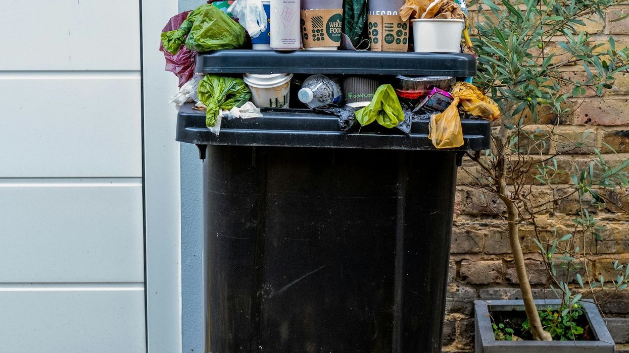 A residential garbage can overflows with plastic bottles and other waste.