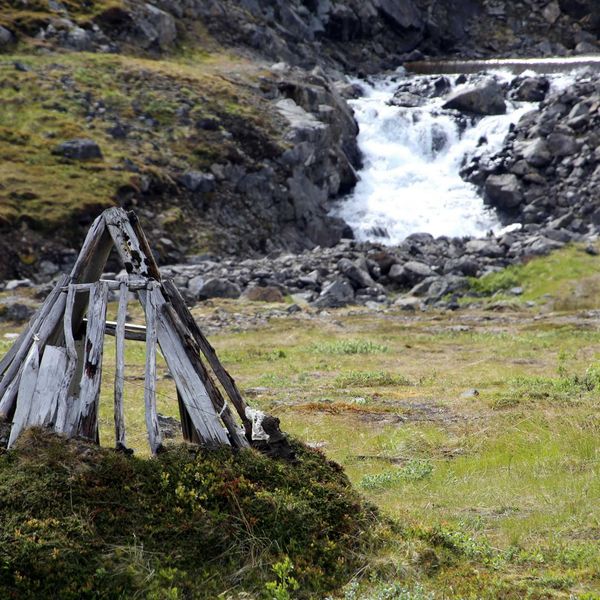 A river running through a green, rocky environment with a small wooden structure in foreground.