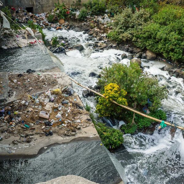 A river with trash along its banks flowing under a bridge.