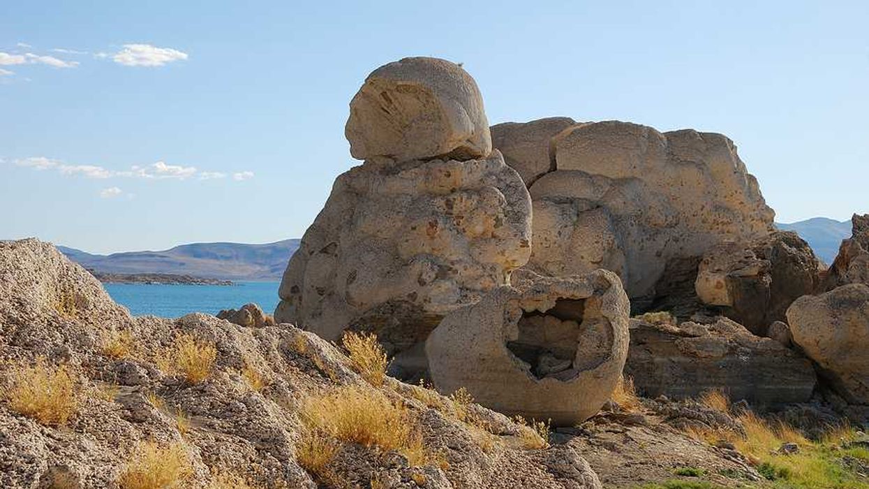 A rock formation in the desert with a lake in the background