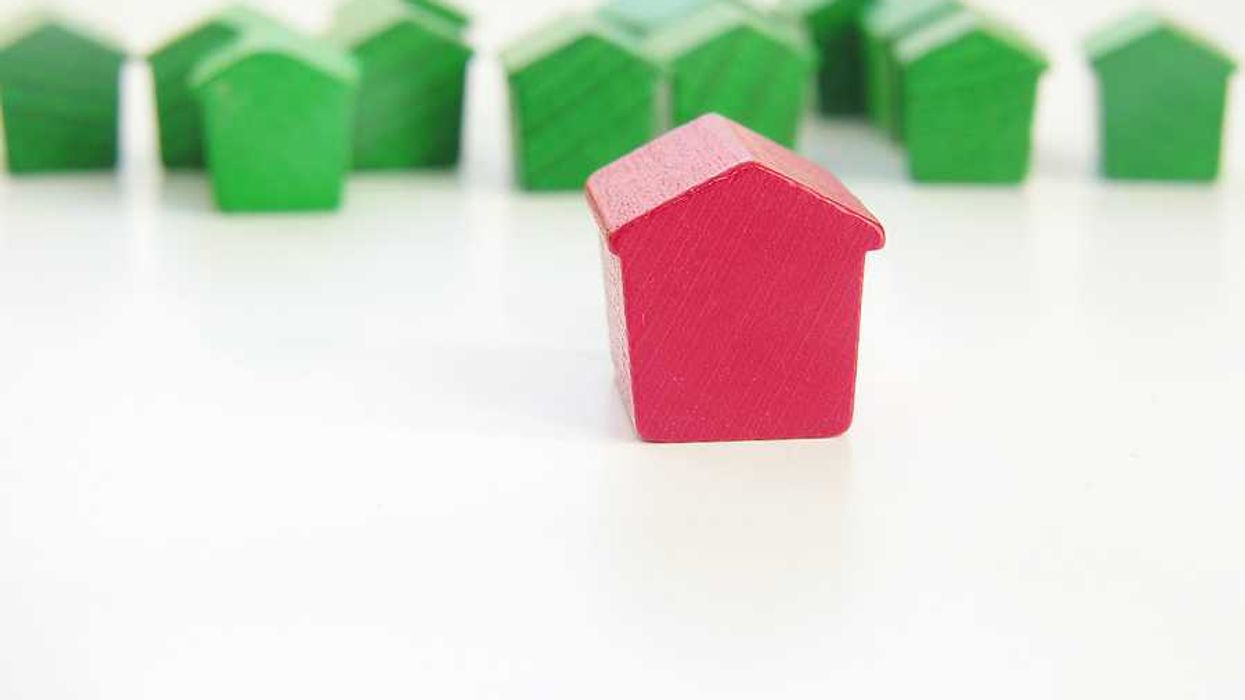 A row of green wooden house models with a red house model in the foreground