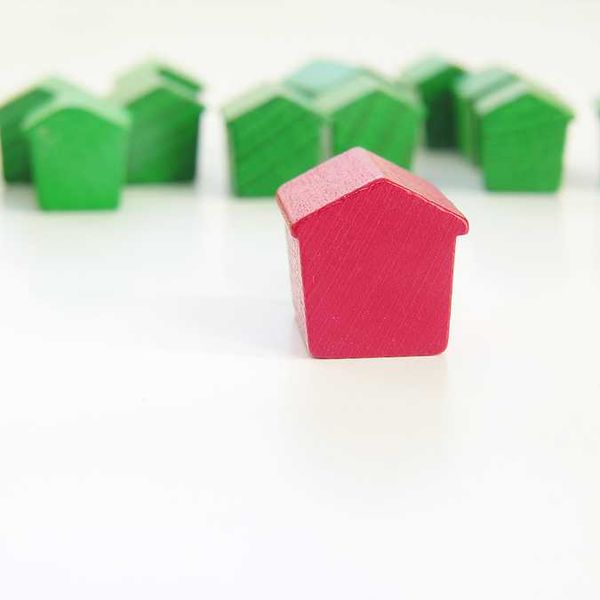 A row of green wooden house models with a red house model in the foreground