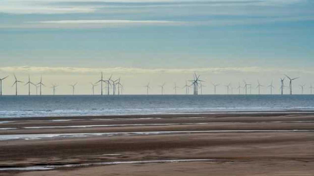 A row of offshore wind turbines viewed from a beach