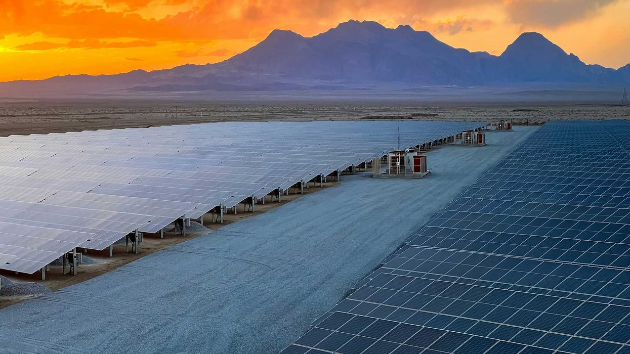 a row of solar panels sitting on top of desert land with mountains and sunset in background.