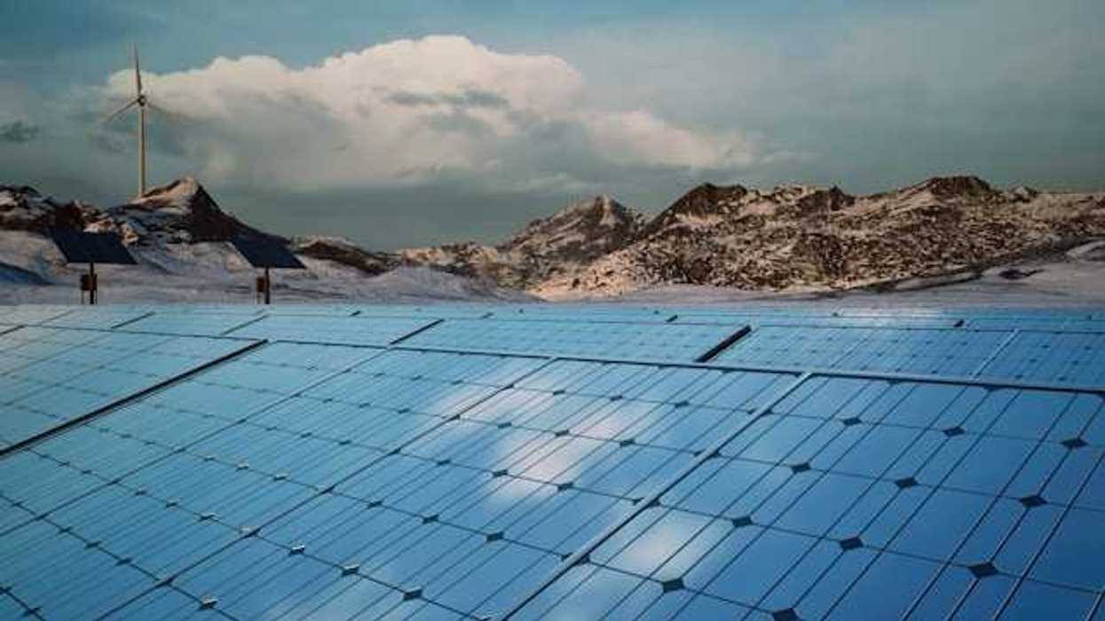 A row of solar panels with mountains and a wind turbine in the background