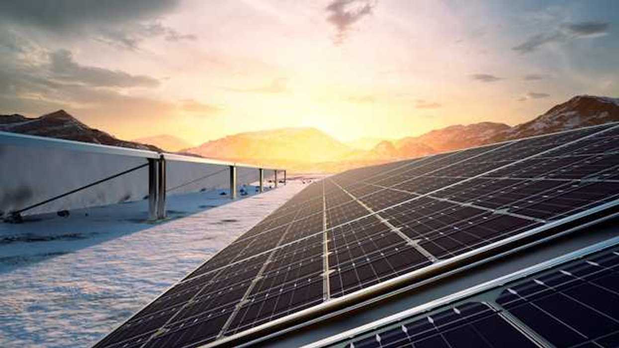 A row of solar panels with the setting sun and a mountain range in the background