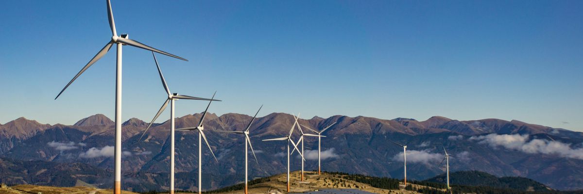 A row of wind turbines and solar panels on a mountainside.