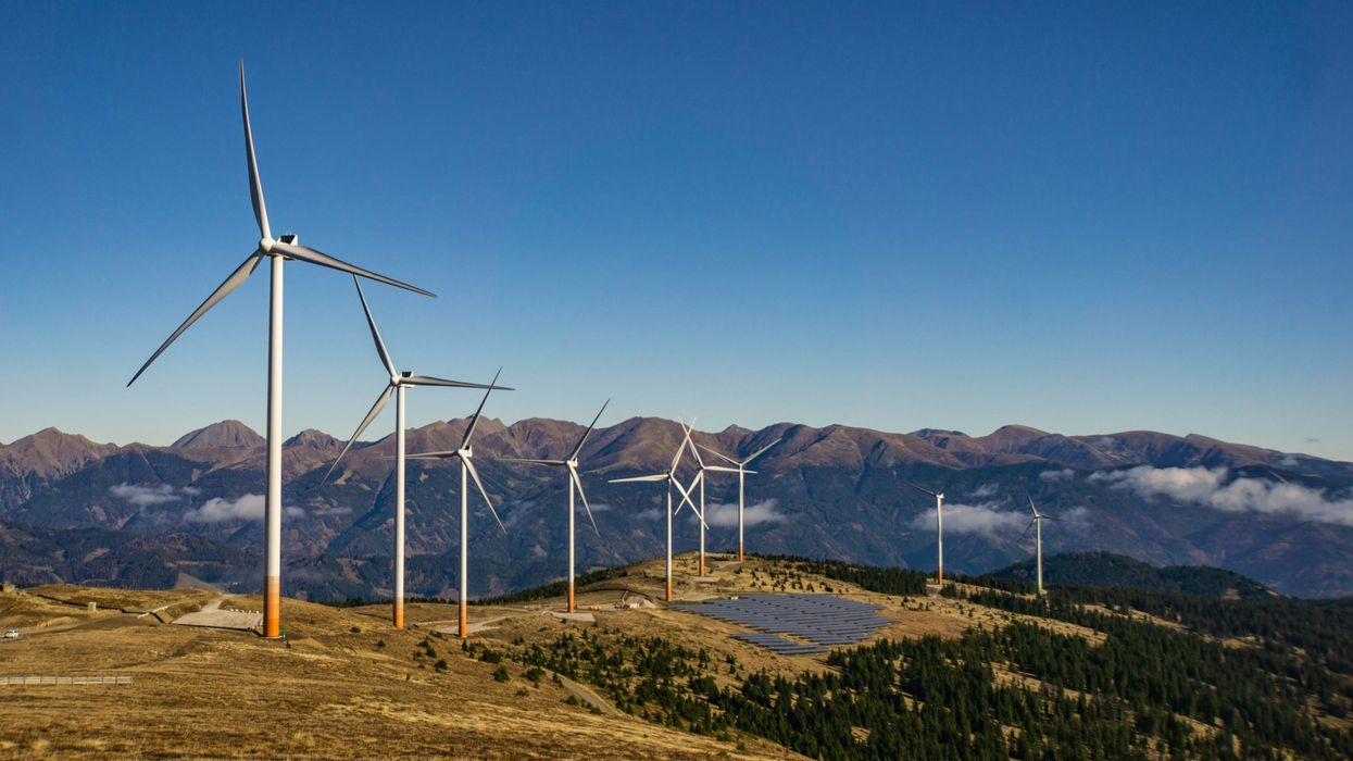 A row of wind turbines and solar panels on a mountainside.