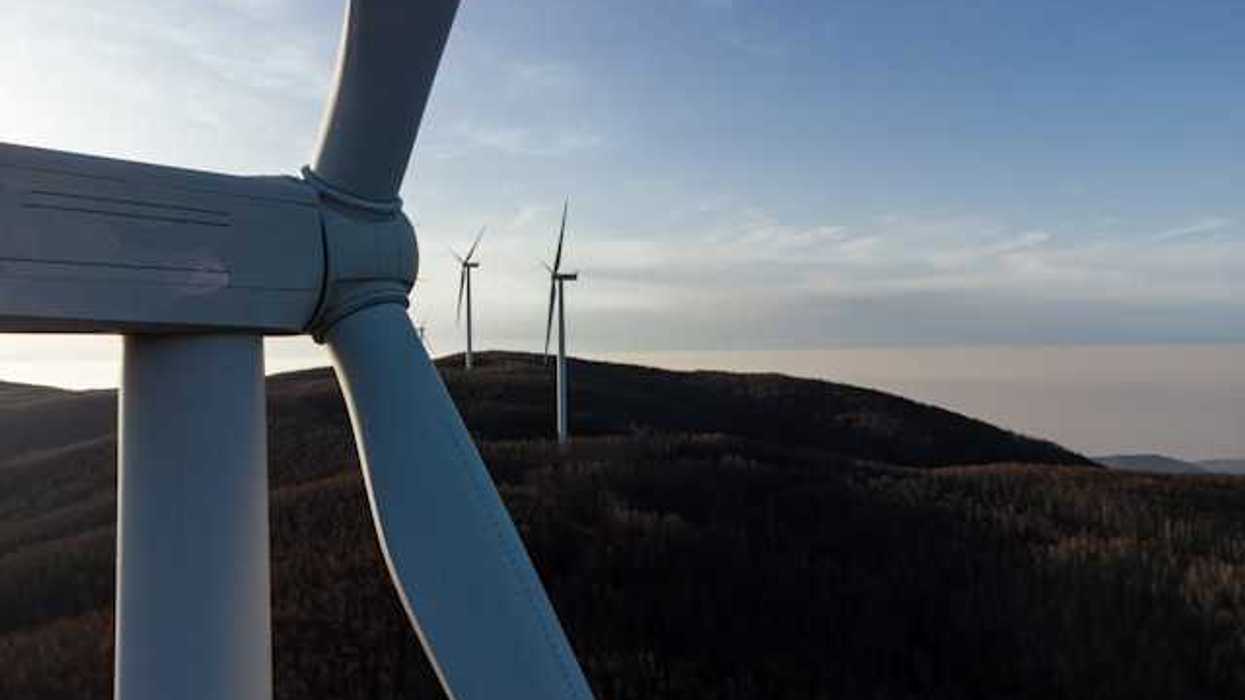 A row of wind turbines at dusk installed on rolling hills