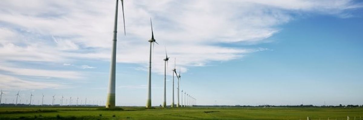 A row of wind turbines in a green field stretching into the distance.