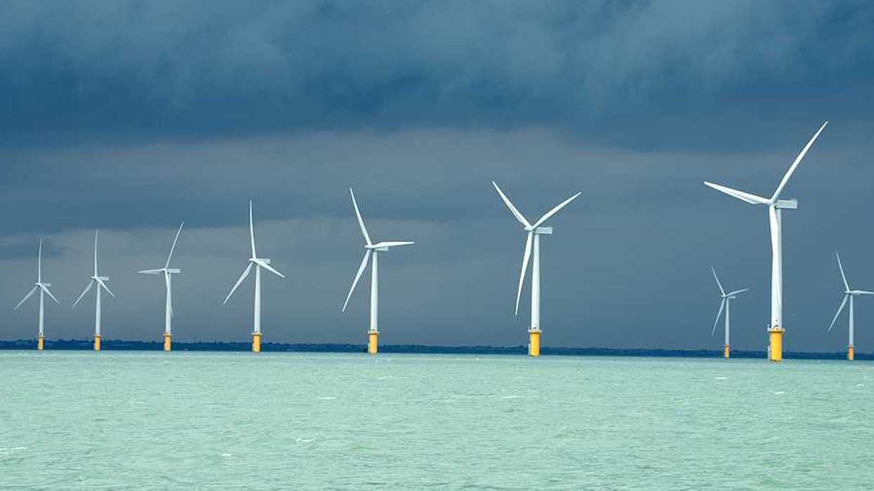 A row of wind turbines in the ocean with dark storm clouds in the distance