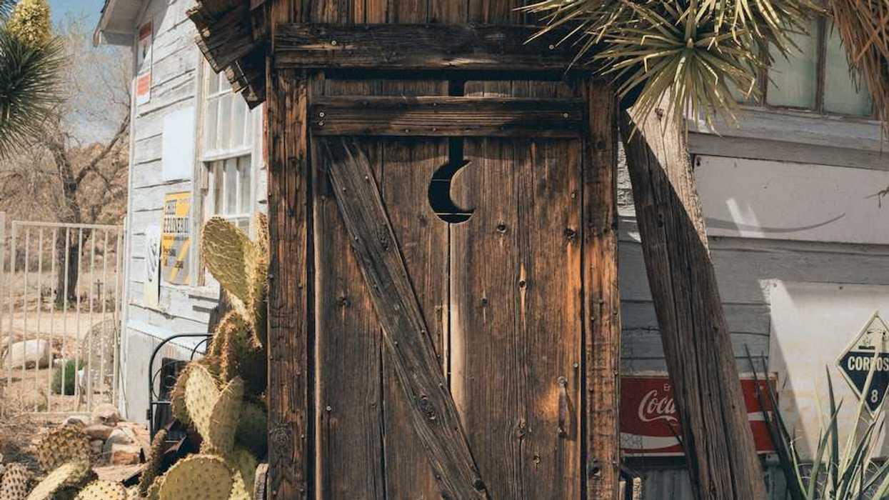 A rustic outhouse with a crescent moon in the door