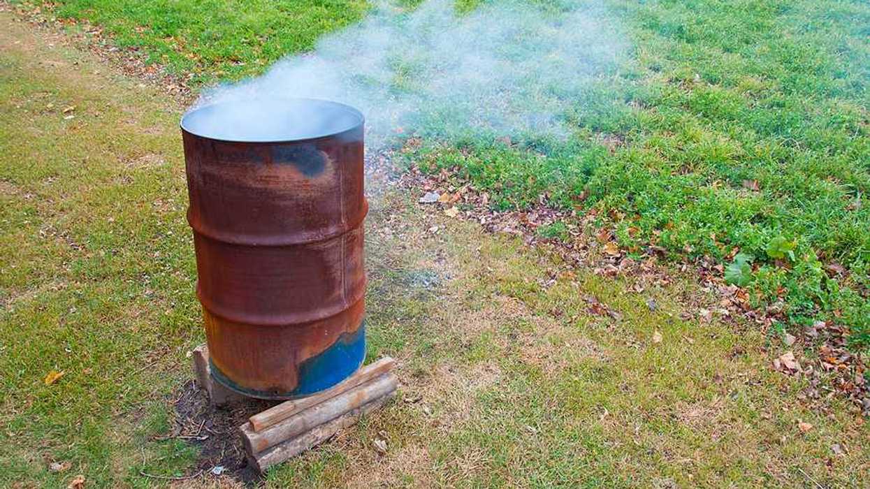 A rusty barrel with burning items in it, smoke billowing from the top